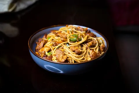 Bowl of stir fried noodles with meat and spring onion