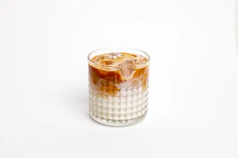 Iced coffee layered over condensed milk in a glass